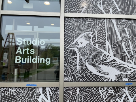 A close-up photo of a window with a bird decal next to a sign that says "Studio Arts Building"