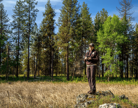 USFWS Biologist Molly Dixon stands on a rock while holding binoculars in her hands