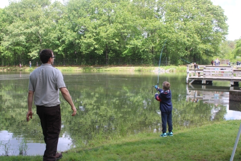 Service employee in refuge browns watches as young boy casts fishing pole into pond.