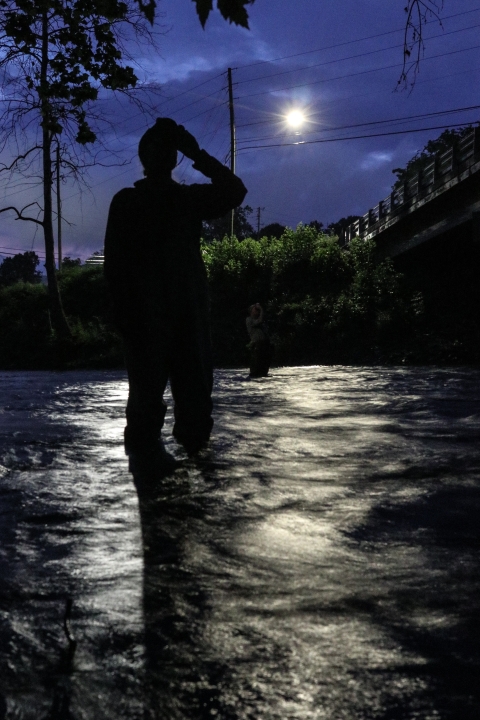 Two people standing in a river, looking through night-vision goggles