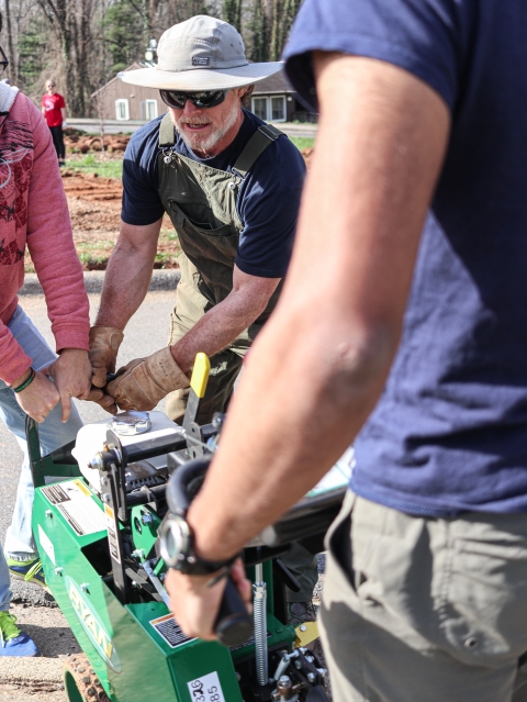 Three people gripping a piece of lawn machinery