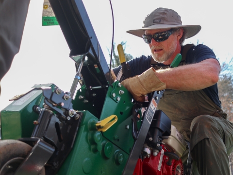 Man, outside, crouched down, working on a piece of machinery