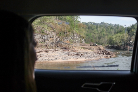Person looking out a car window at a river with heavy machinery beside it