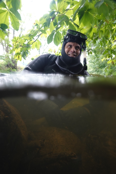 Biologists in a wet suit, mask on top of his head, sits in shallow water