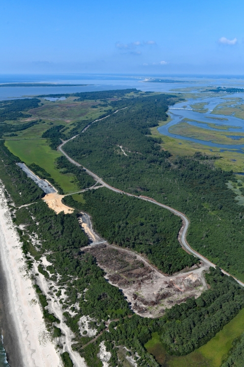 An aerial view of a road and parking lots under construction among the trees.