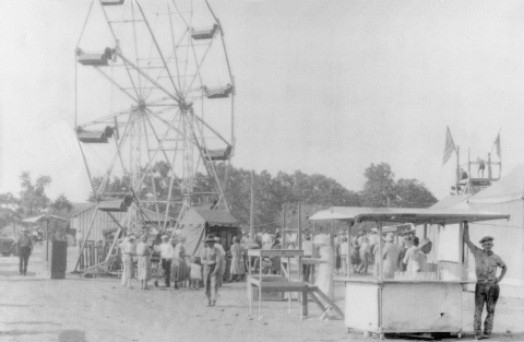 a black and white image of a small fair with stands and a ferris wheel