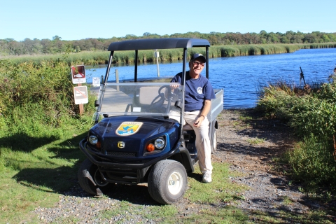 A smiling volunteer sits in the drivers seat of a golf cart
