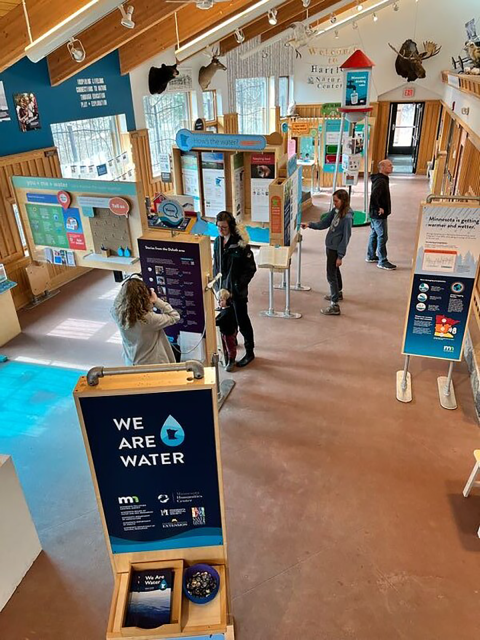 From a birds eye view, panels and exhibit pieces are places throughout a large open building. People are milling about. 