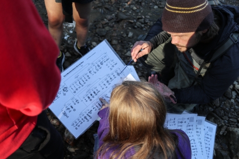 Man kneeling with students, one of whom is holding a piece of paper with illustrations of invertebrates