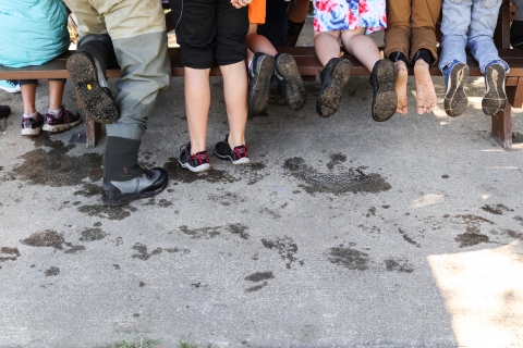 Legs and feet of several people standing beside a picnic table or kneeling on the table's bench seat