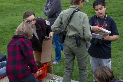 A Fish and Wildlife Biologist in a USFWS uniform works with youth participants of an outreach event in a large public lawn.