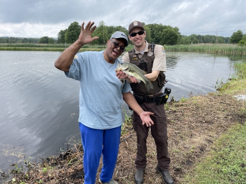 Law Enforcement Officer Mike McMenamin poses with a veteran and the bass he caught at the Veterans' Fishing Derby at Wallkill River National Wildlife Refuge
