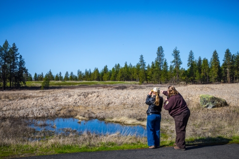 A FWS employee points to a bird in the distance while a member of the public looks through binoculars