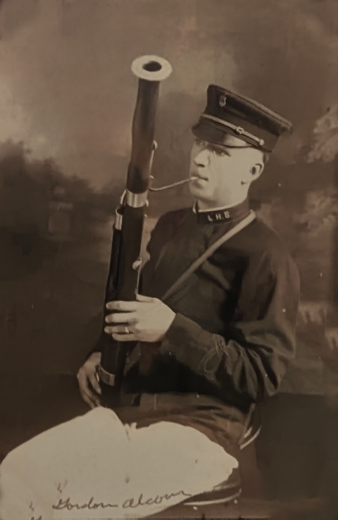 Sepia photo of a young man in band uniform cap and jacket, playing a bassoon.