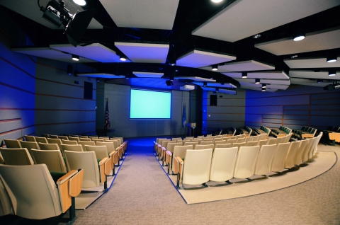 Room filled with seats in rows facing a large empty screen with blue lighting