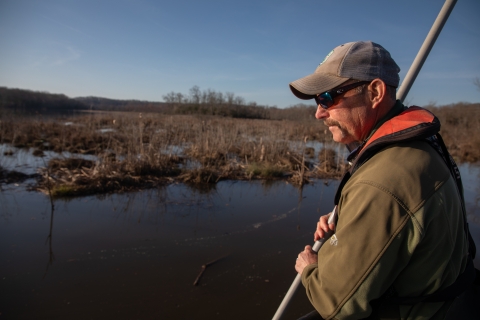 Biologist stands on the front of a boat with net to catch fish. 