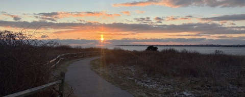 View of trail at sunset, with sun setting in horizon over an ocean.