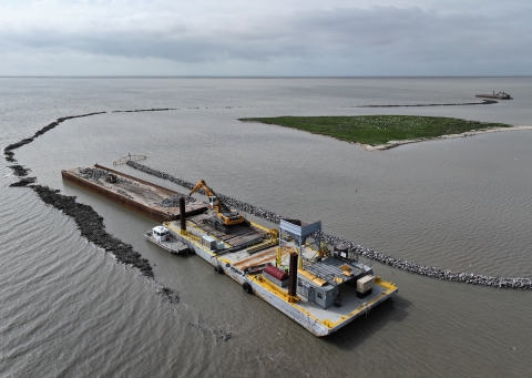 A barge floats between a row of limestone rocks a row of dark colored rocks, near Dressing Point Island.