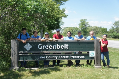 Youth Conservation Corps volunteers standing behind a sign for the Greenbelt Forest Preserve in North Chicago, Illinois.