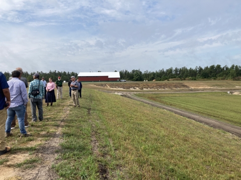 A group of people standing in an open field with cranberry marshes in the background where cranberries are being cultivated.