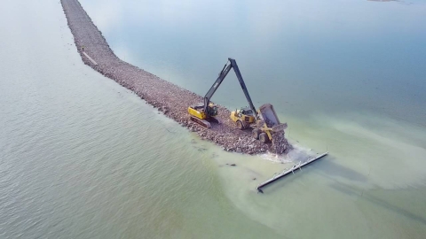 Aerial view of a breakwater being built in open water one dump load at a time.
