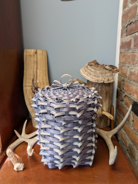 A small lilac and silver colored weaved basket.