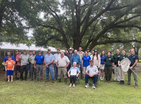 A large group of people pose for a photo outside in front of a large tree.