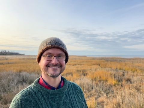 Man in green sweater and brown hat standing in an open field