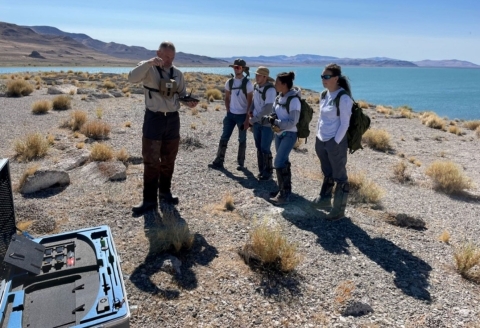 Refuge staff instructs the Youth Conservation Corps teens about drone usage for Anaho Island NWR surveys while standing on the refuge with lake behind.