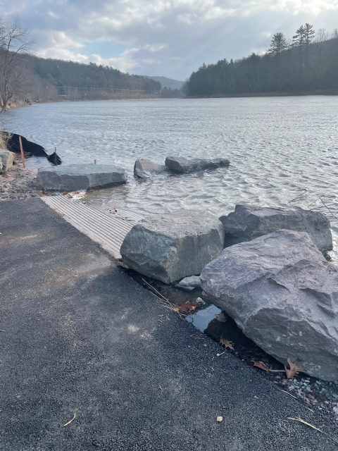 A paved boat ramp meeting a river, with large boulders to either side to diffuse wave energy