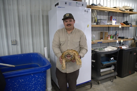 Person holding a large turtle in a facility with storage equipment and tanks