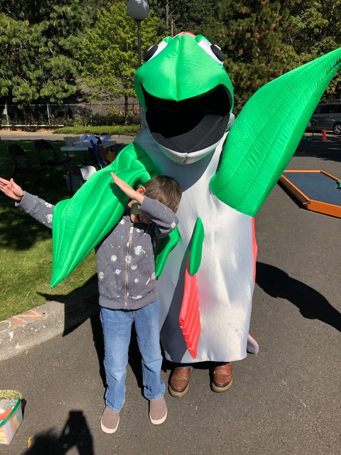 A costume of a large salmon character poses smiling with a small child