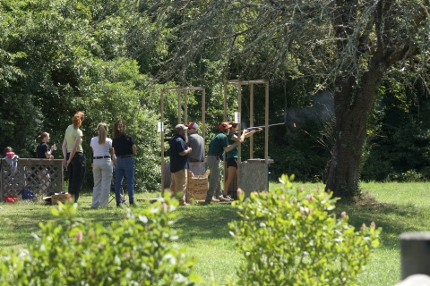 Group of target shooters behind shooting stand watch a target shooter aim at clays. 