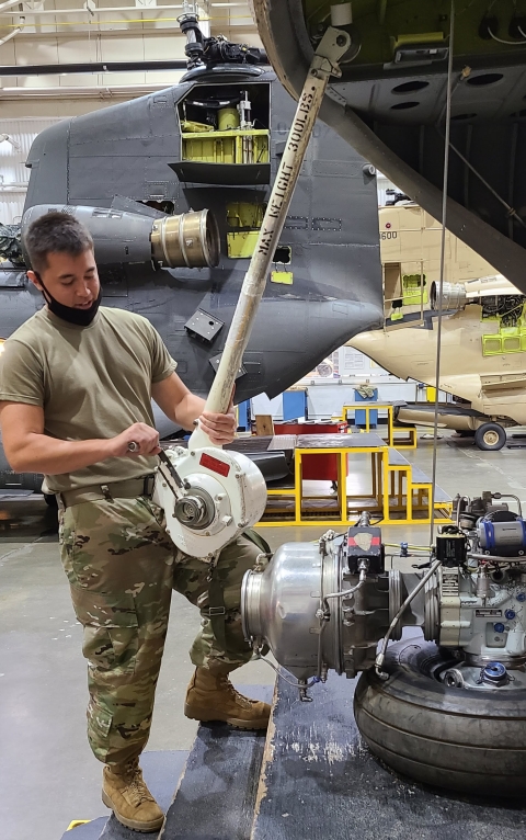 Author, Addison Emerson, working on helicopter repairs in a military base hanger. Other Chinook helicopters in the background.