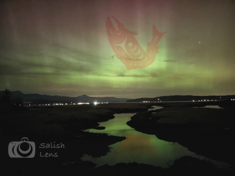 Image of the northern lights over the Skokomish River and Hood Canal. A tribal "line art" depiction of a jumping salmon is integrated into the northern lights by the photographer, Addison Emerson. 