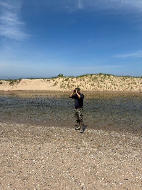 A man standing on a beach looking through binoculars away from the water.