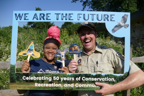 Refuge employee and young student smile in front of grassy background.