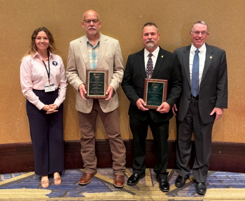 4 people pose; middle 2 with plaques