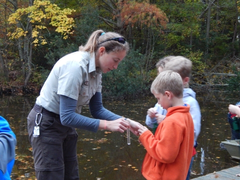Refuge employee handing a vial of water to a student as they stand on a dock.