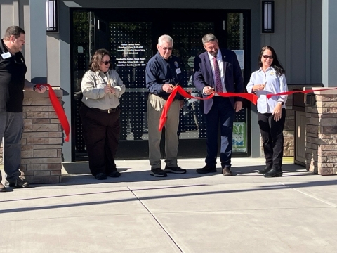 Men and women hold scissors to cut a large red ribbon.