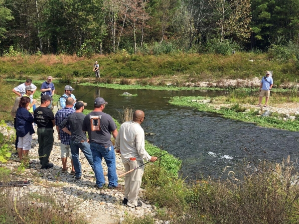A group of students gathers around an instructor on the bank of a creek.