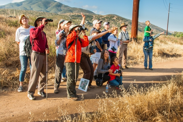A Service employee leads a group on a hike; the attendees look through binoculars at wildlife