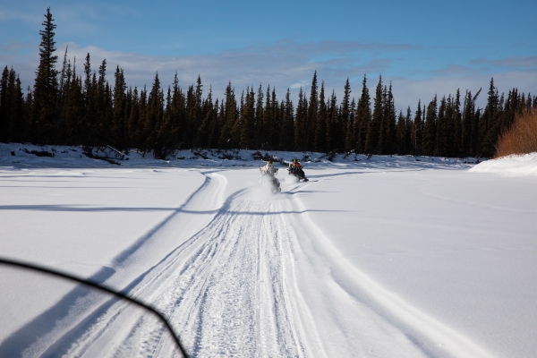 A photo shot from a snowmobile following two other rides who create tracks in the white snow ahead