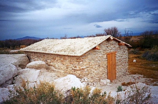 A very old white stone cabin with wooden door in a rocky landscape