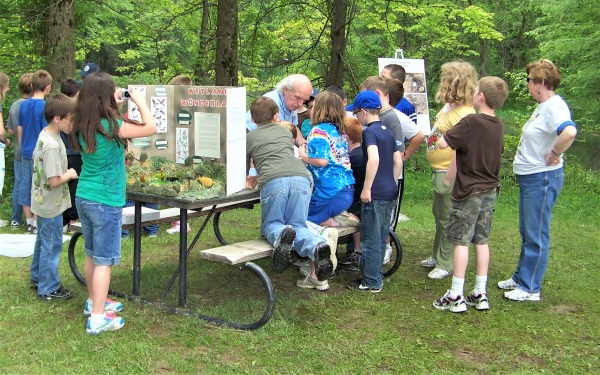 School group outside around wetland display listening to Refuge volunteer