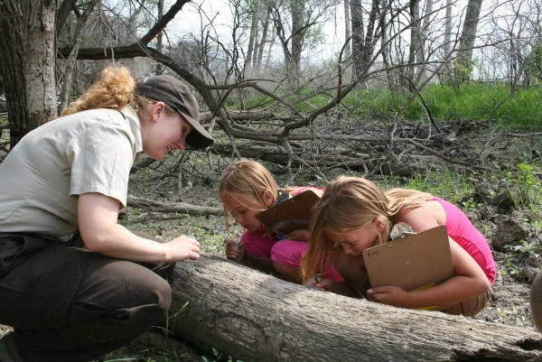 A refuge ranger investigating a log with two students.