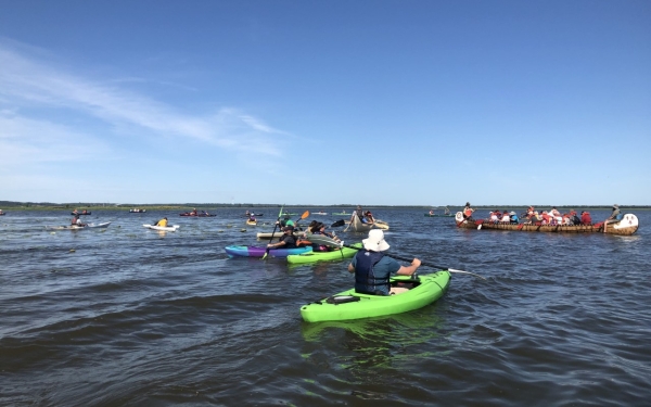 several kayak paddlers on open water near a larger fourteen passenger canoe