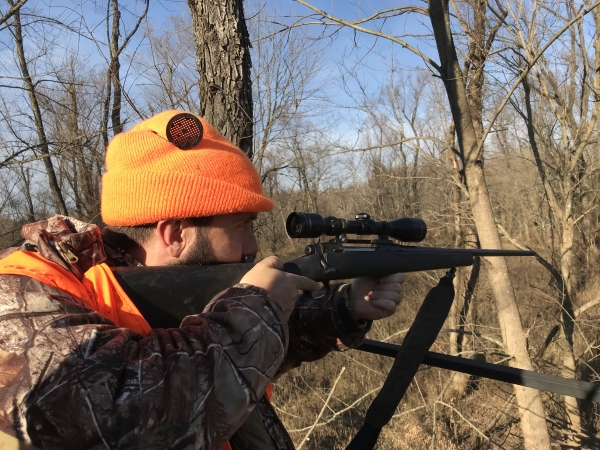 An image of a hunter in a tree stand with their rifle. 