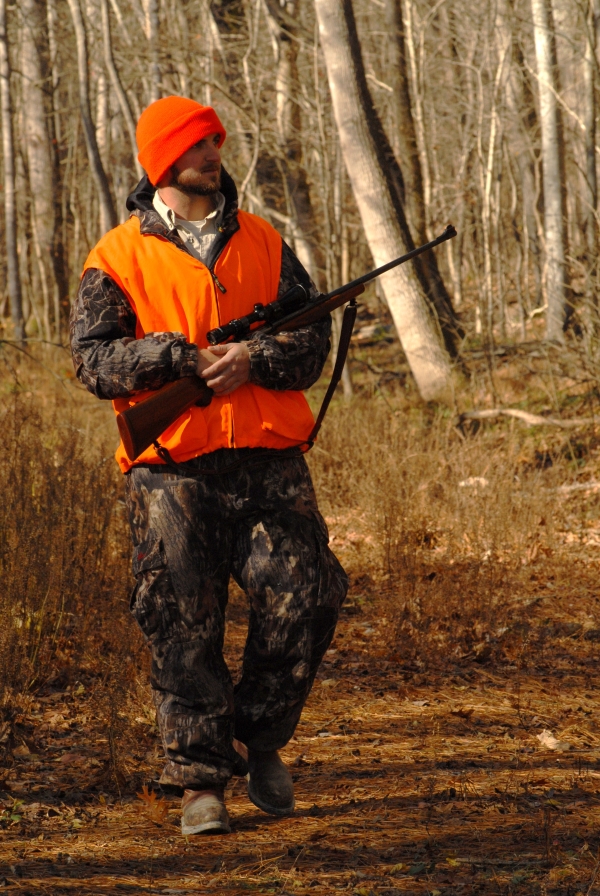 An image of a hunter walking in the woods with their rifle. 