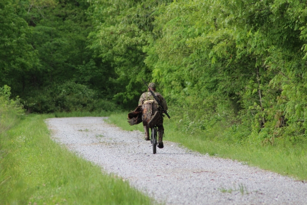 An image of a turkey hunter riding a bike down a gravel road to get to their hunting location.